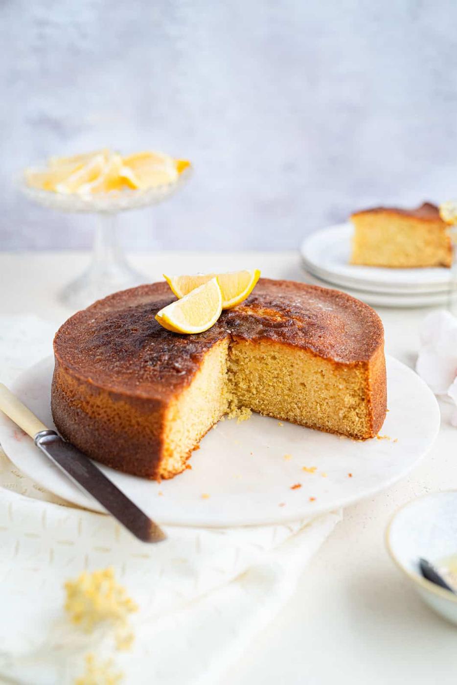 Lemon drizzle cake with slice taken out on a marble cake plate