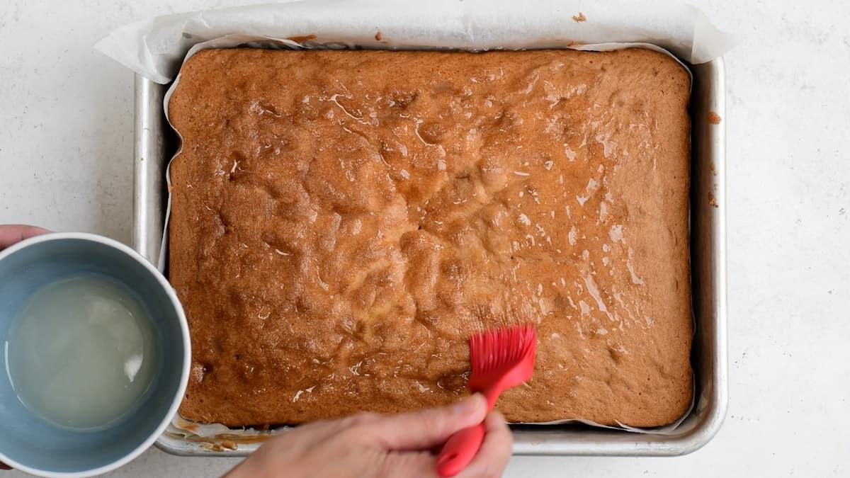brushing lemon syrup over lemon traybake