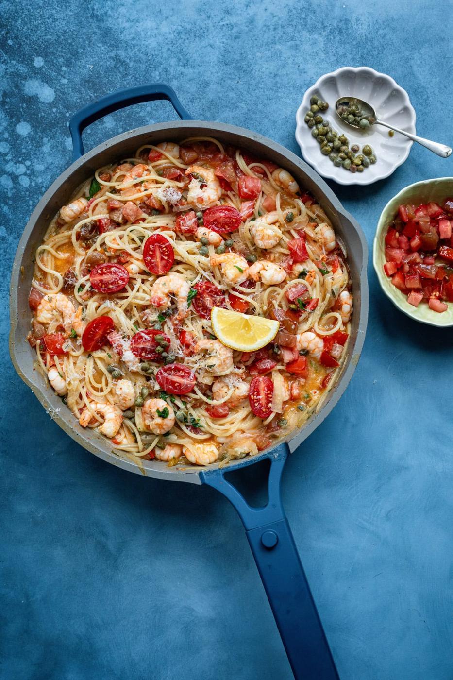 overhead shot of a pan with lemon garlic shrimp spaghetti, small bowls of diced tomatoes and capers on the side