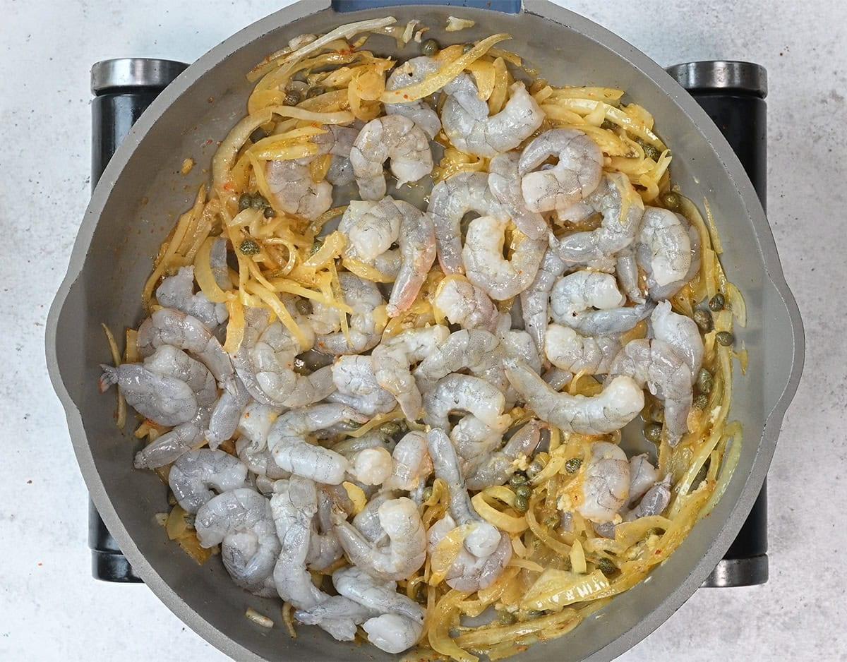 shrimp cooking with sliced onions and garlic in a pan