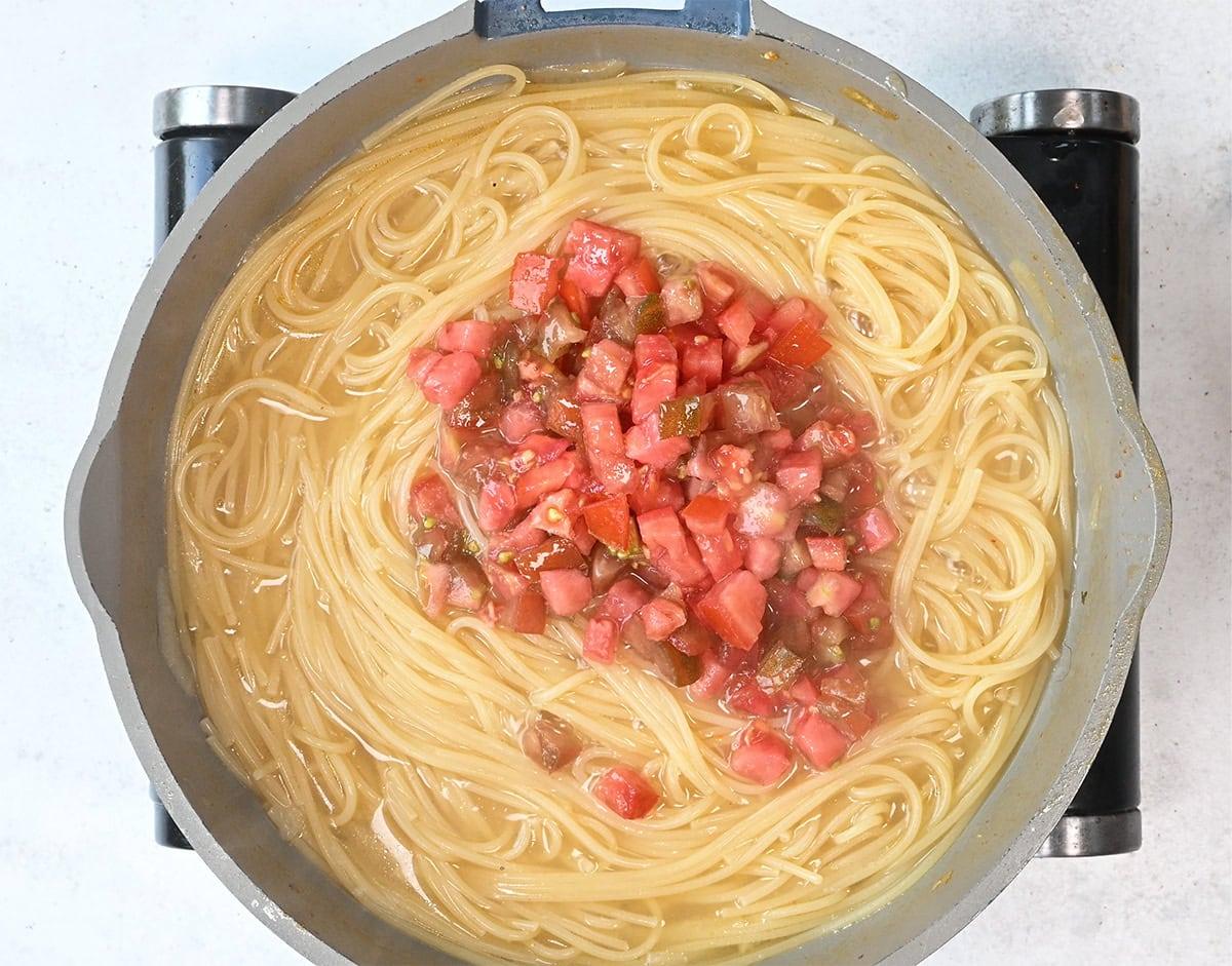 spaghetti cooking in a pan topped with fresh diced tomatoes