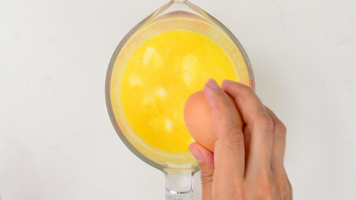 cracking a en egg into a measuring jug of melted butter and milk