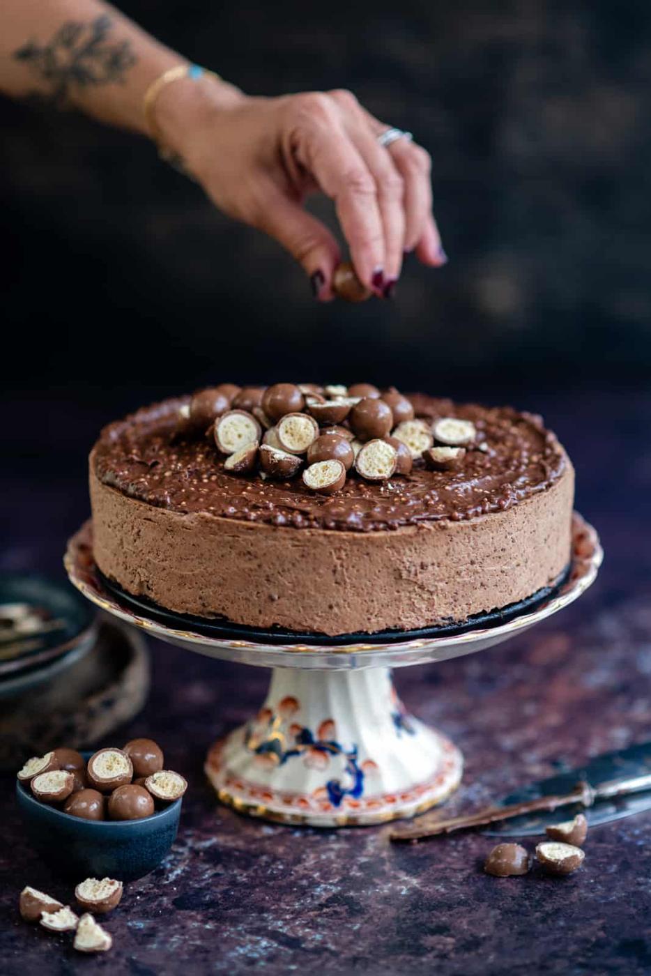 Malteser cheesecake topped with chopped Maltesers on a cake stand