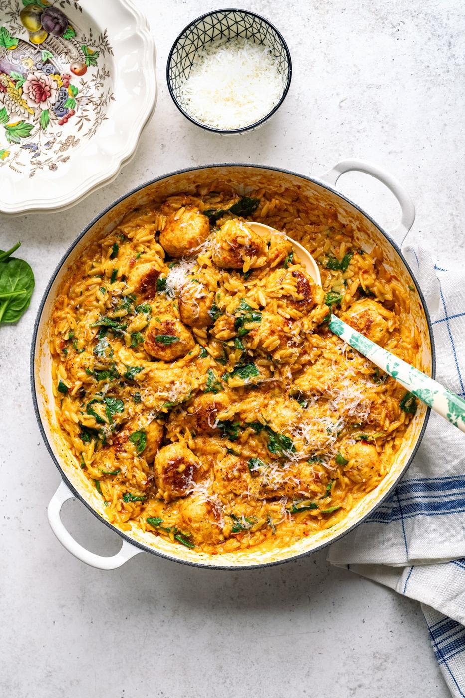 Overhead view of a casserole with Marry Me chicken meatballs with orzo pasta garnished with grated Parmesan