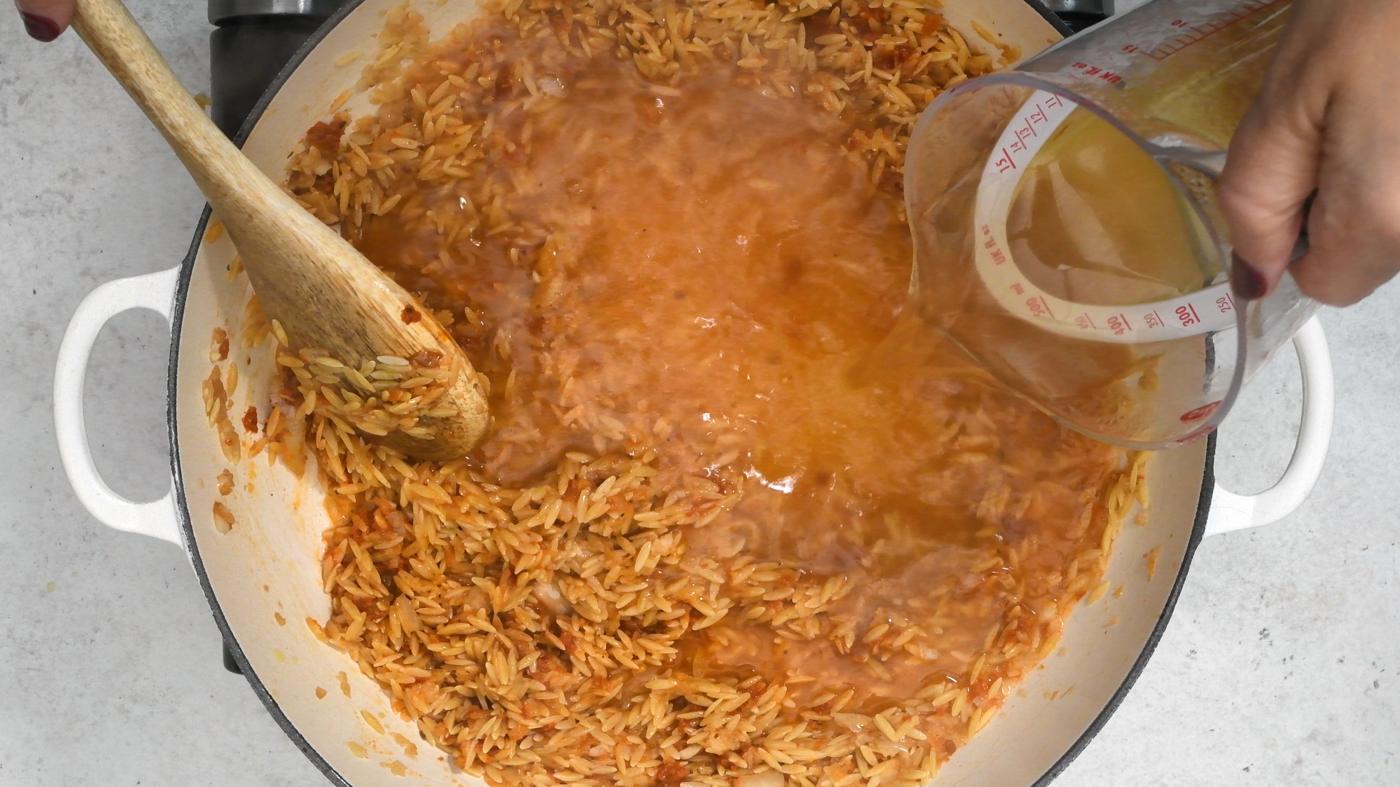 adding chicken broth to a pan of orzo pasta