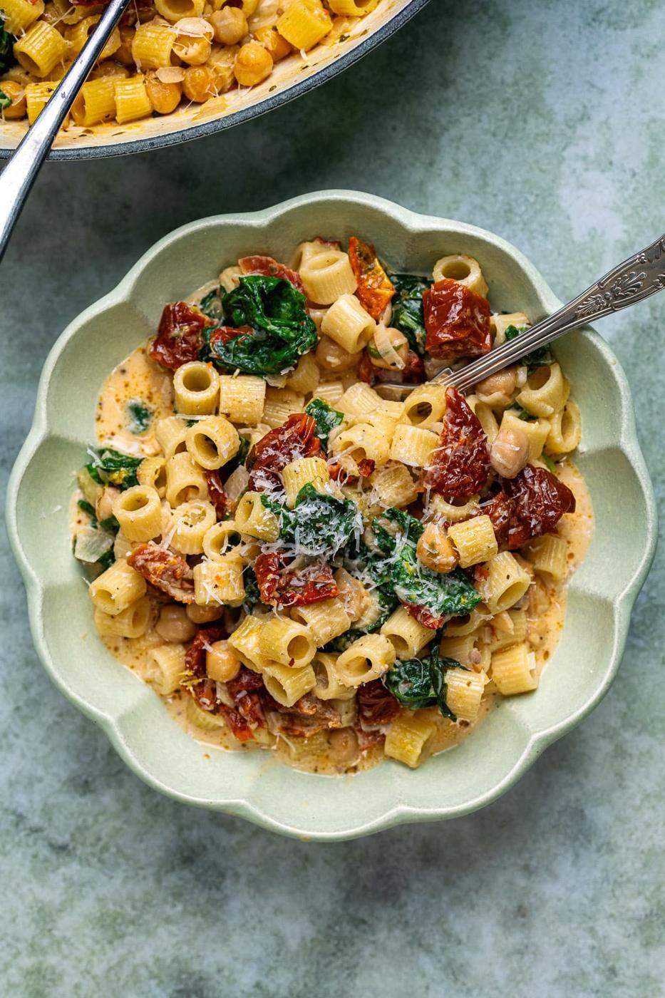 Bowl serving of pasta dish with chickpeas, sun-dried tomatoes in a creamy sauce with Parmesan and spinach