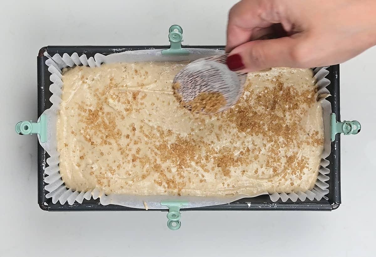 sprinking banana bread batter with Demerara sugar in a loaf pan
