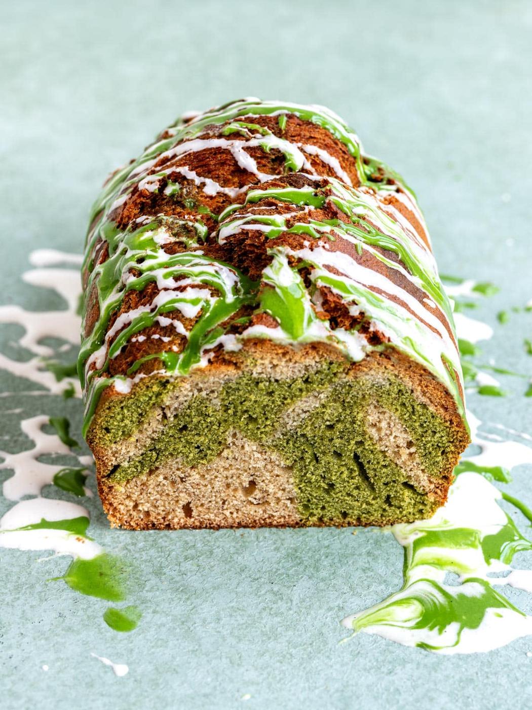 A loaf of marbled matcha banana bread drizzled with white and green icing.