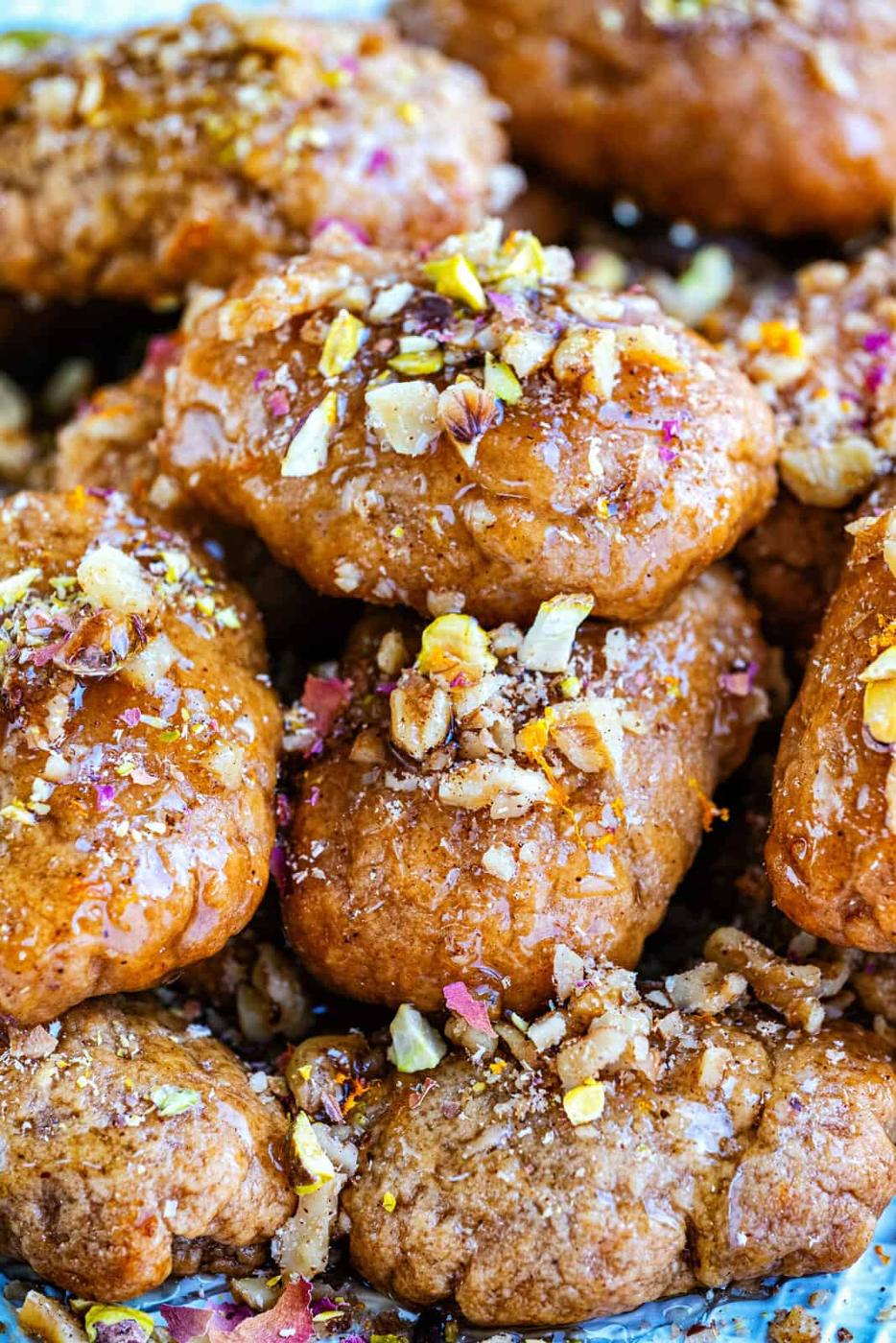 A close-up of golden-brown Greek Christmas Honey Cookies, known as melomakarona, stacked together, topped with chopped nuts and glistening with syrup.