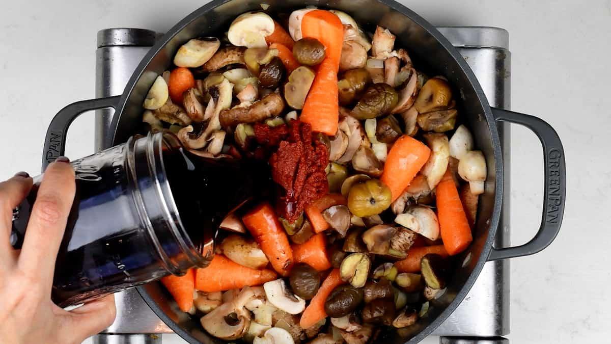 adding wine to a vegan bourguignon in a pot