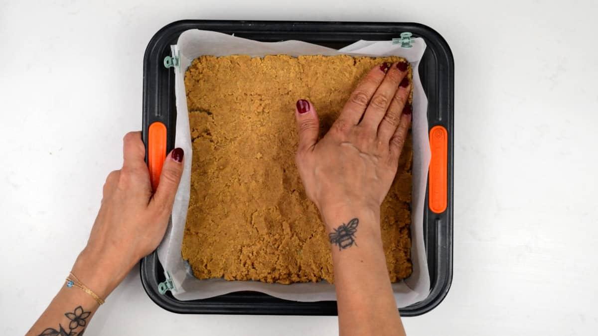 pressing cookie crust into square lined baking tin for cheesecake