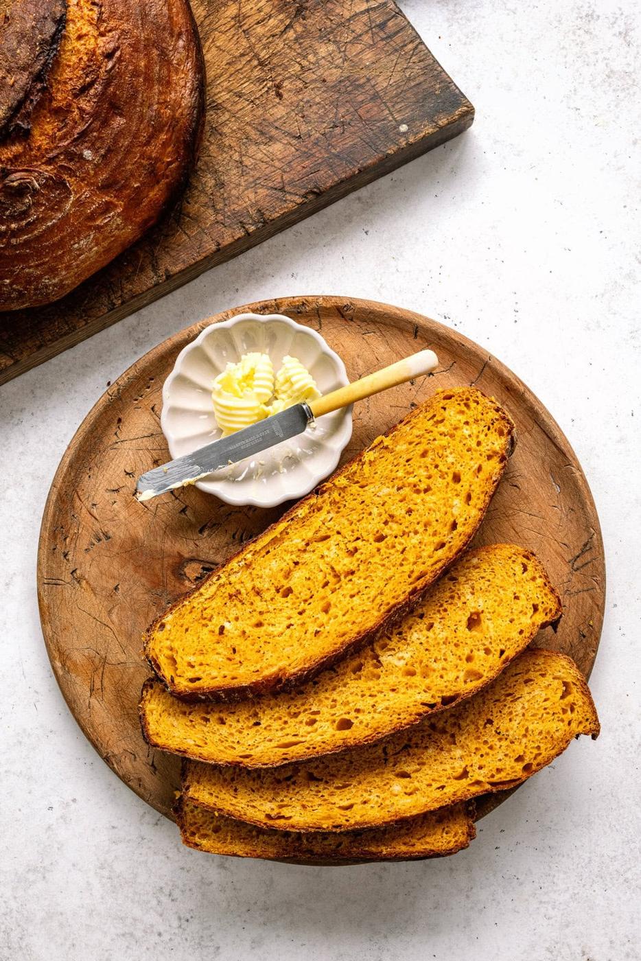 three slices of pumpkin bread on a wooden serving plate, butter on the side
