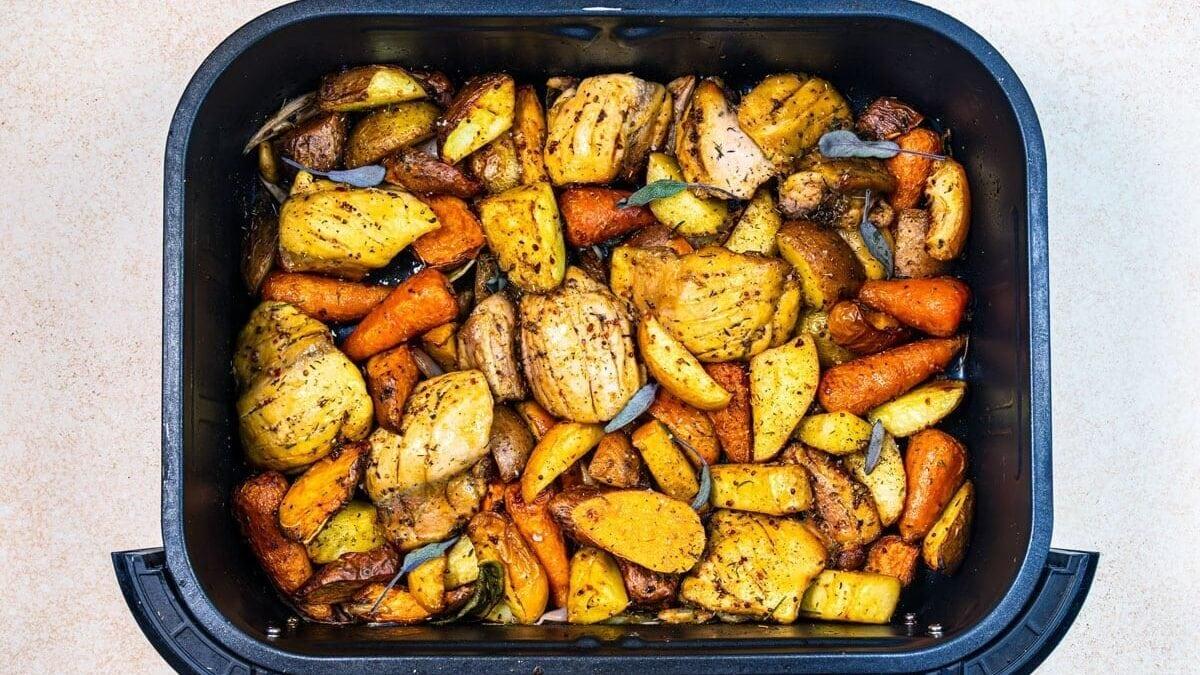 Chopped seasoned potatoes, carrots, and onions roasted in an air fryer basket, garnished with herbs.