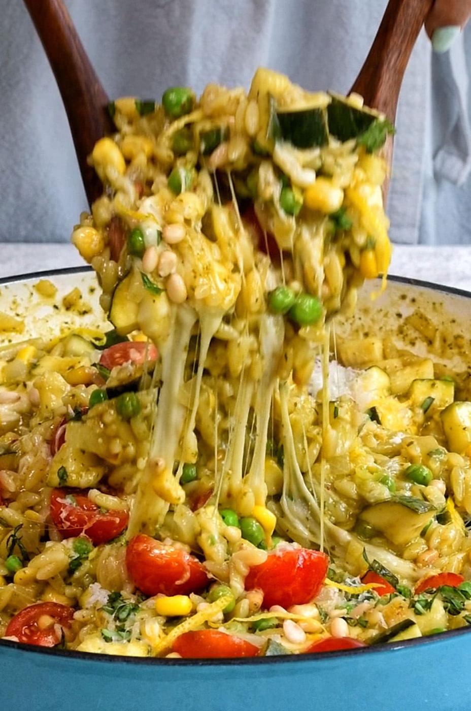 Scoopful lifted out of a pan or pesto orzo with cheesy pull from the mozzarella
