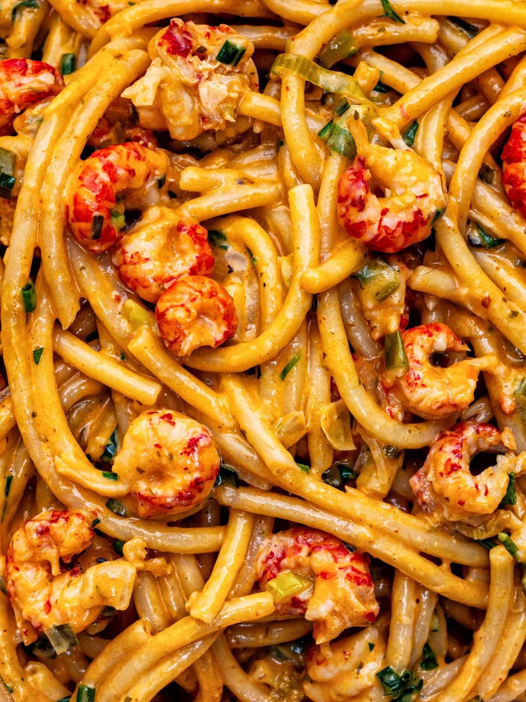 Close-up of creamy crayfish pasta mixed with tender crayfish pieces and chopped green herbs, all coated in a rich, orange-coloured sauce.