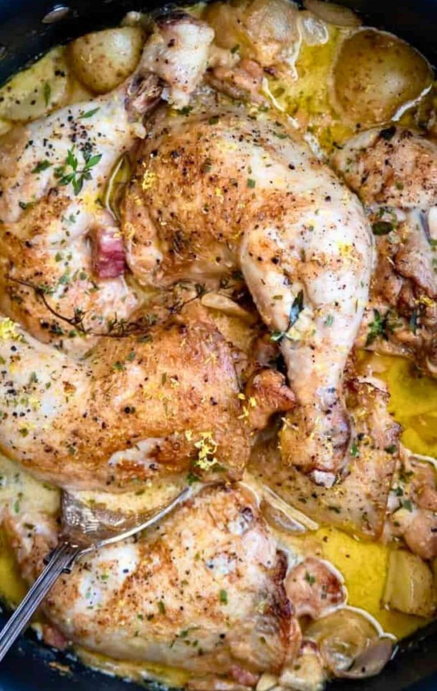 Cooked chicken legs and thighs in a creamy, seasoned sauce with herbs and lemon zest, served in a pan. This creamy chicken casserole features a spoon resting in the rich sauce among tender chicken pieces.