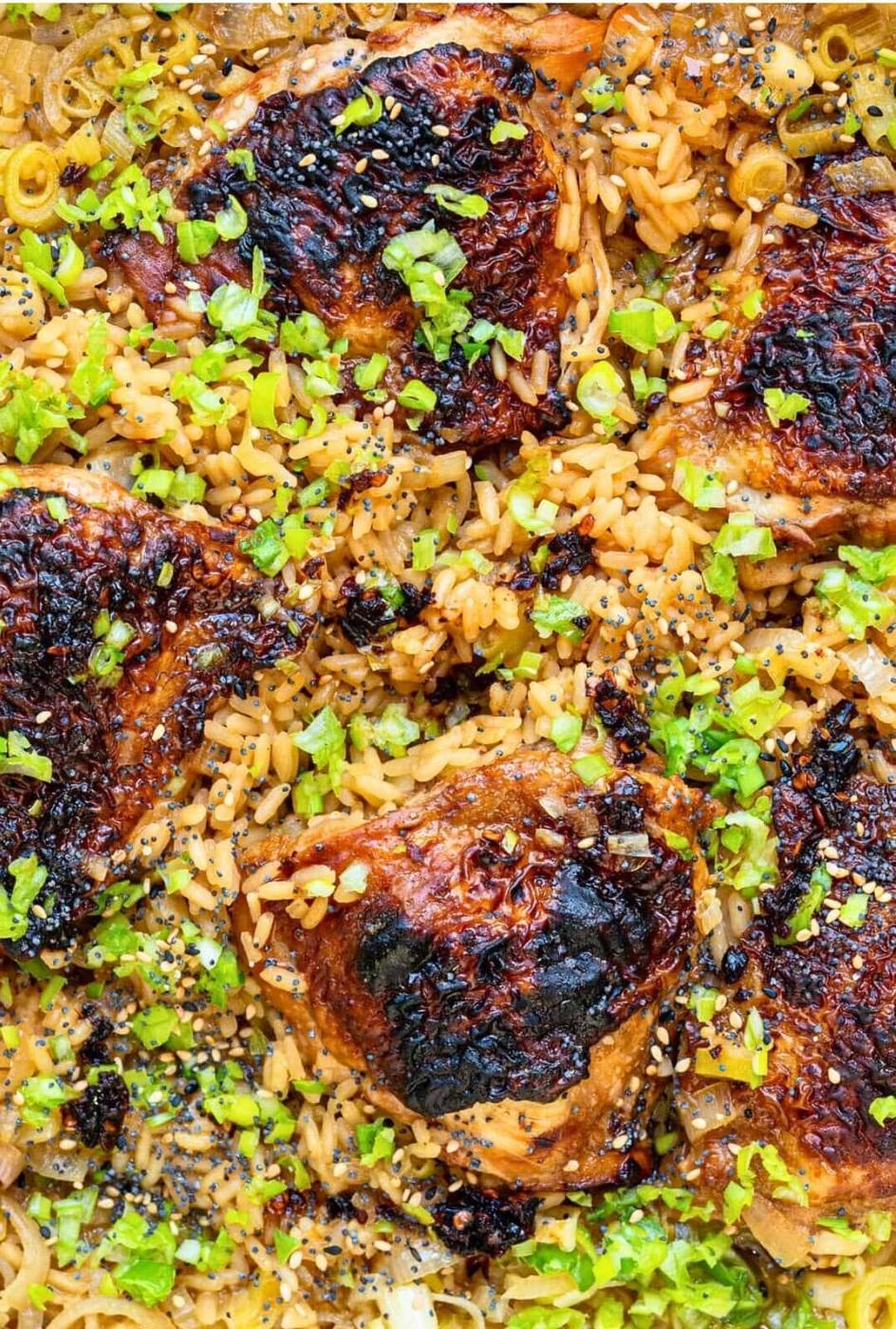 Close-up of Miso Chicken and Rice featuring baked chicken thighs with crispy, browned skin on golden rice, garnished with chopped green herbs and poppy seeds. The dish appears savory and well-seasoned.