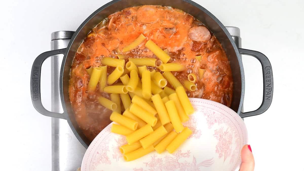 Cooking rigatoni pasta in a pot of tomato sauce and stock