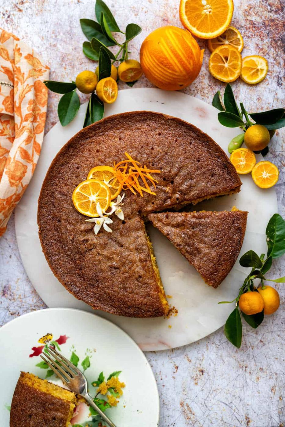 Orange drizzle cake decorated with orange slices on ceramic platter with slice cut out
