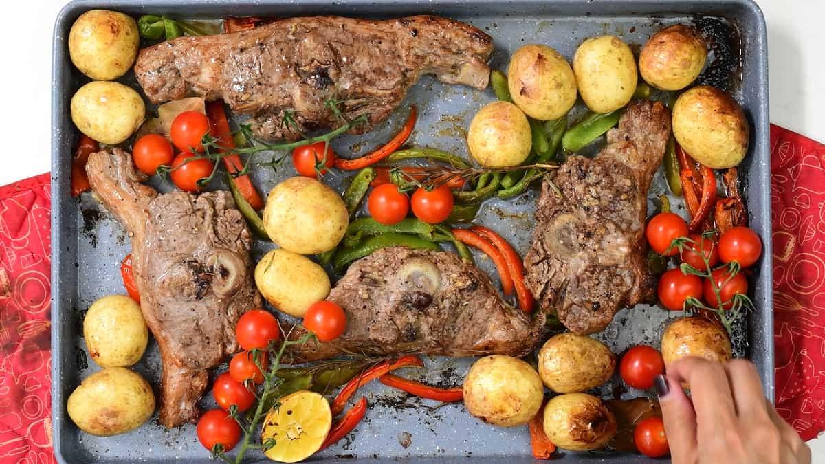 adding tomatoes to oven baked chops in roasting tin