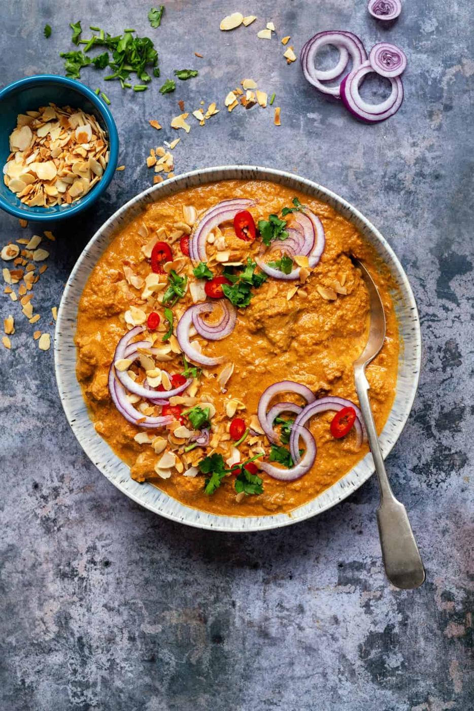 Bowl of creamy lamb pasanda with toasted flaked almonds, coriander and chilli garnish