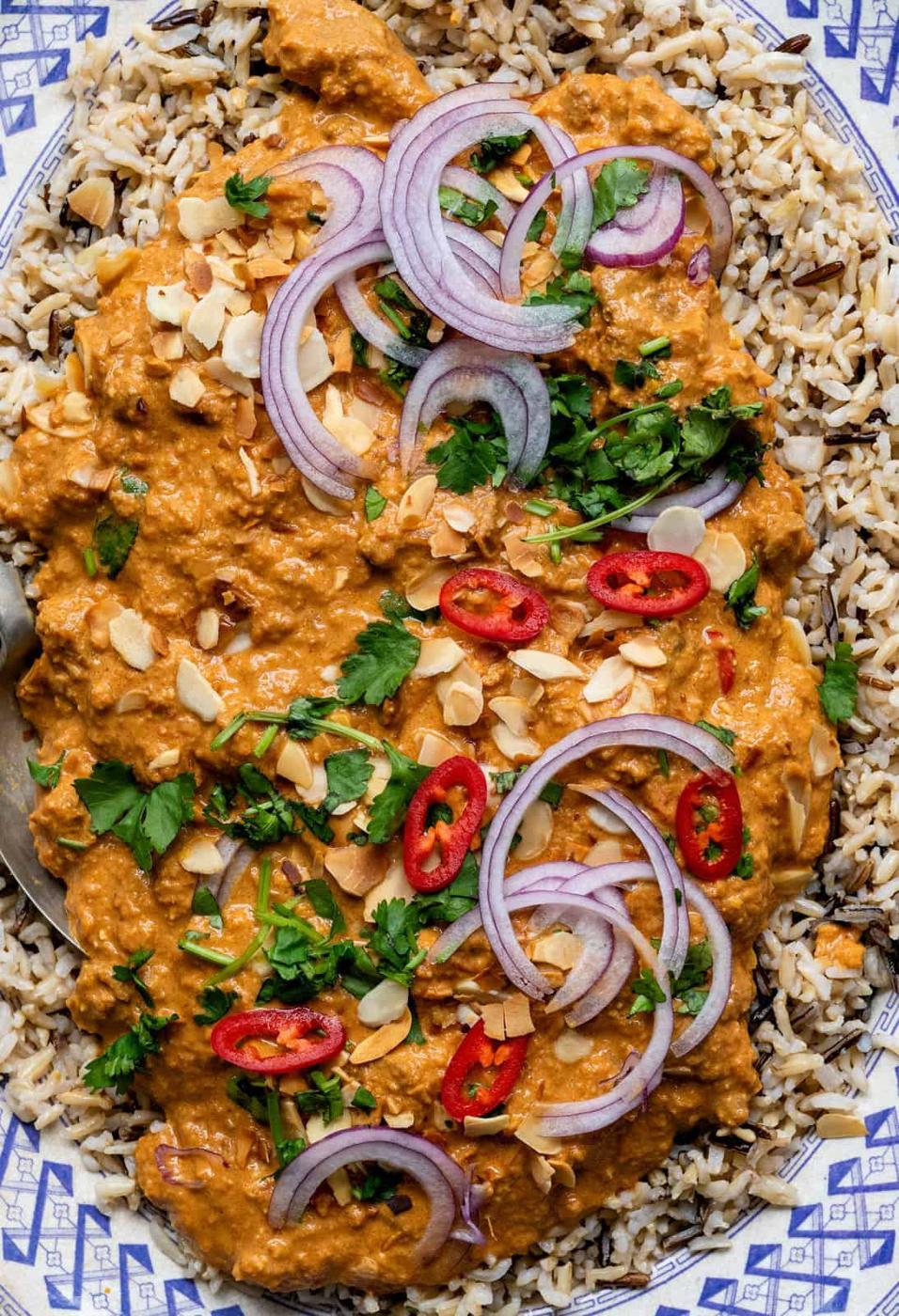 close up on a platter of lamb curry garnished with coriander, onions and diced chilli