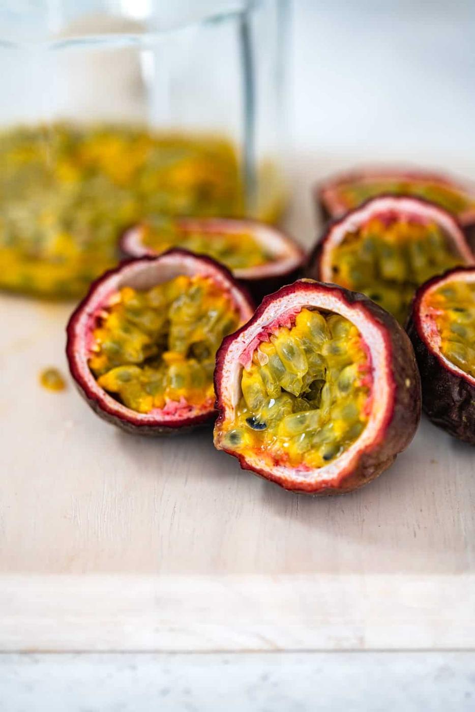 Several halved passion fruits with bright yellow-green, seedy pulp are displayed on a light wooden surface, hinting at the fresh ingredients perfect for making vibrant Passion Fruit Jam. More pulp and fruit appear blurred in the background.