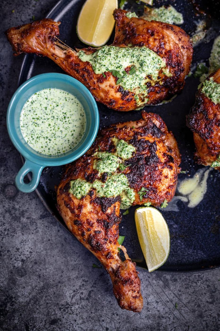 close up or roast chicken leg served with green sauce and lime wedges