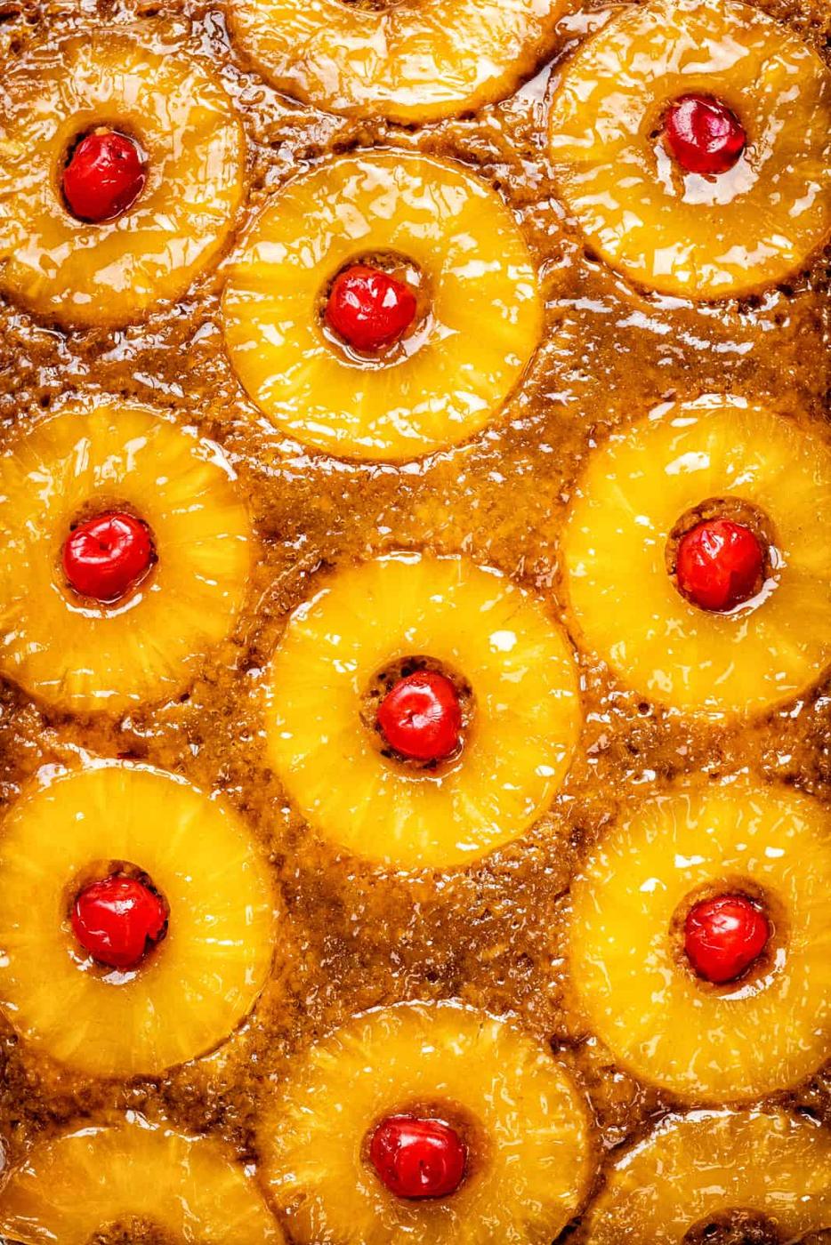 Close-up of a Pineapple Upside Down Cake topped with glossy pineapple rings and bright red maraschino cherries in each center, showcasing its caramelized, mouthwatering surface.