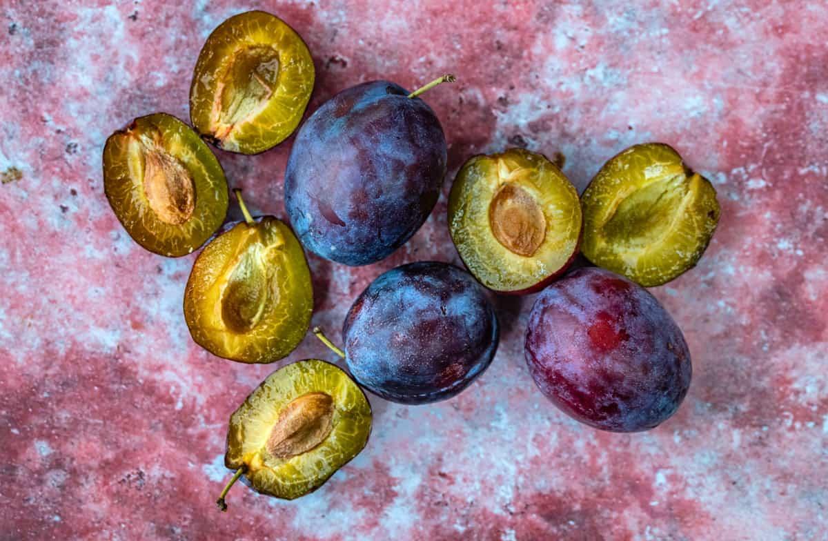 whole and sliced plums on a pink background