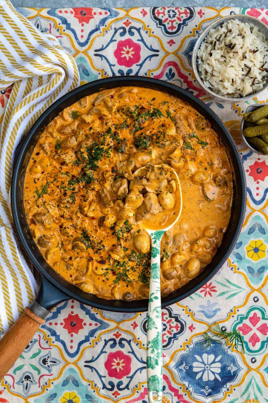 Pork stroganoff in a skillet with rice bowl on the side