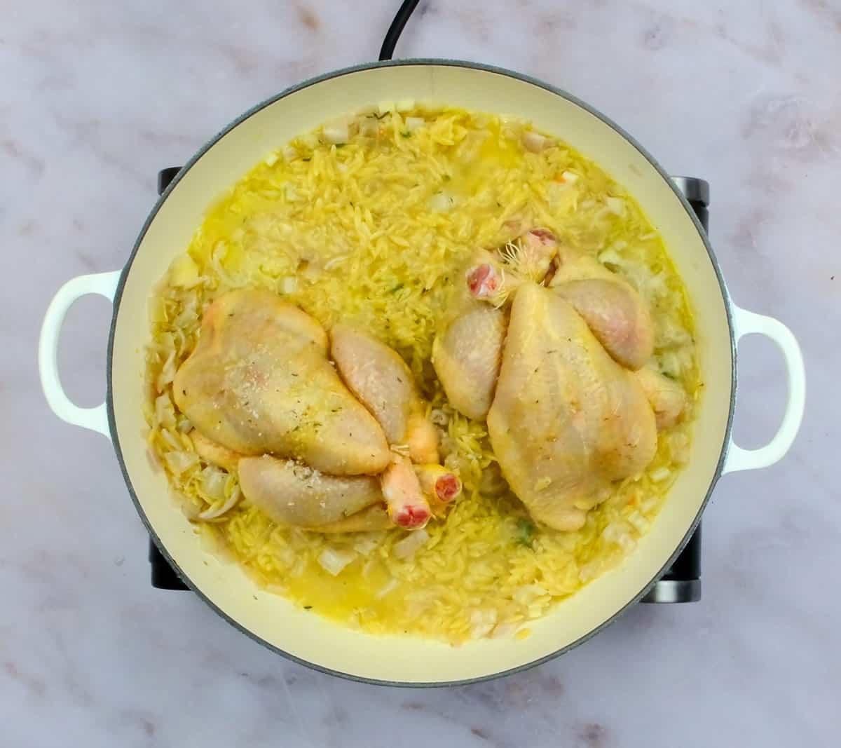 Two poussin chicken on top of orzo in a shallow casserole dish