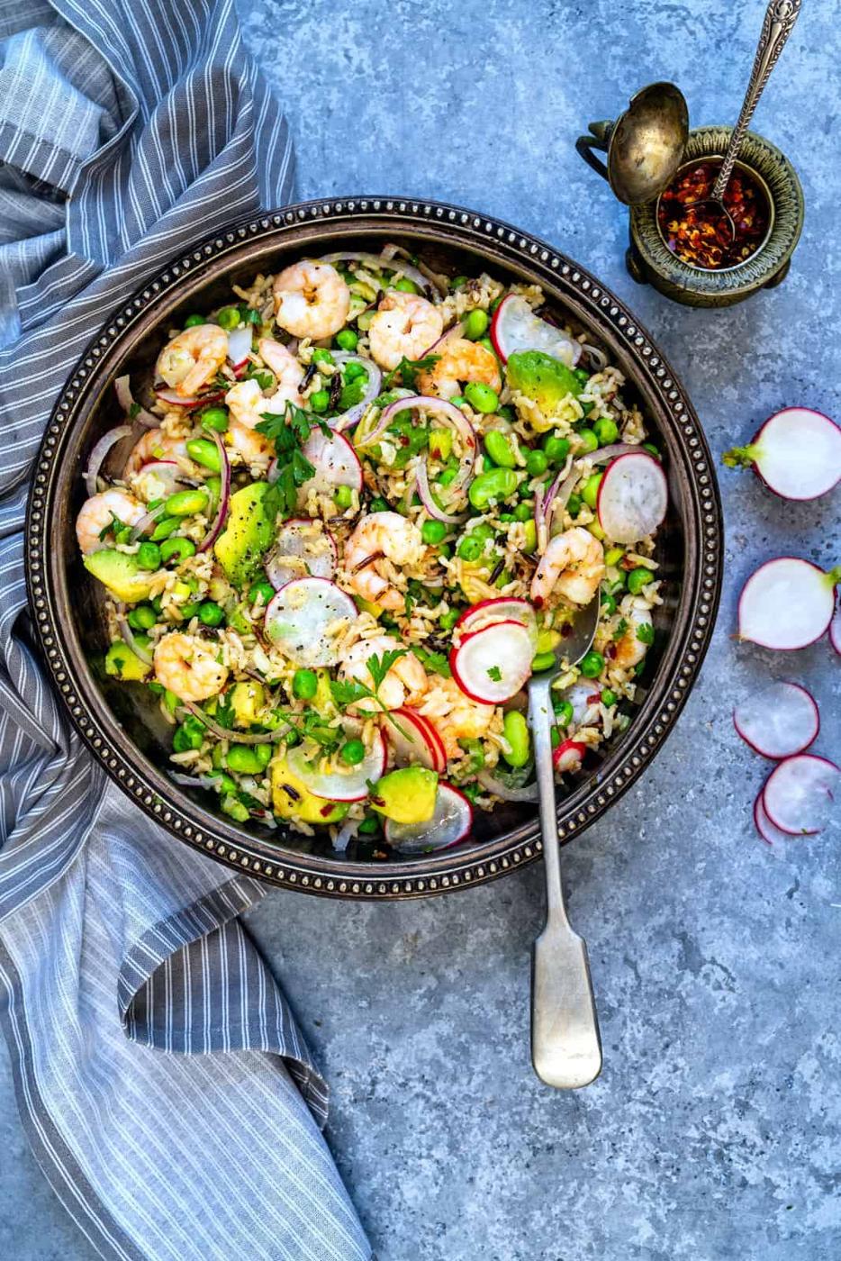 Overhead view of a bowl serving of prawn salad with rice, avocados, radishes and peas