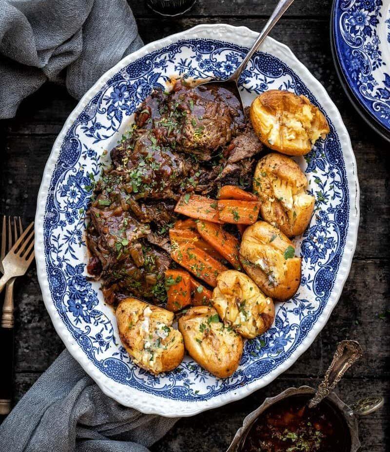Sliced balsamic beef brisket arranged on a blue platter with potatoes and carrots