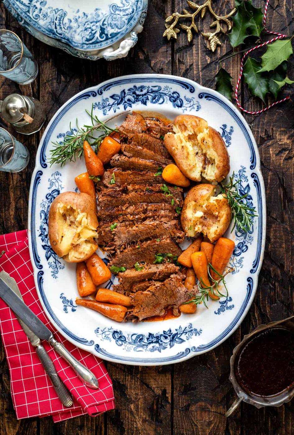 Close up of sliced balsamic beef brisket arranged on a blue platter with potatoes and carrots