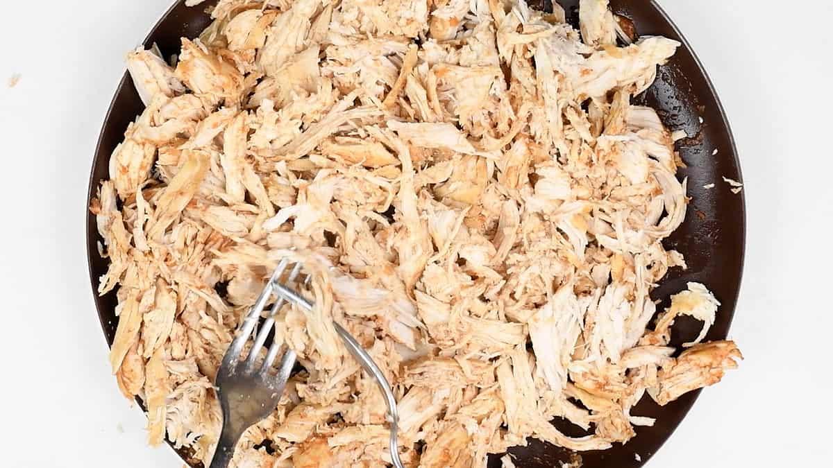 chicken breasts on a plate being shredded with two forks