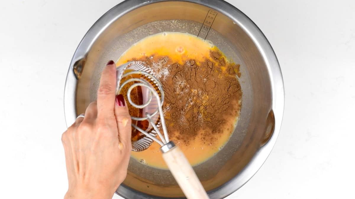 Pumpkin puree, honey and warm spices being whisked into the starter and water in a metal mixing bowl.