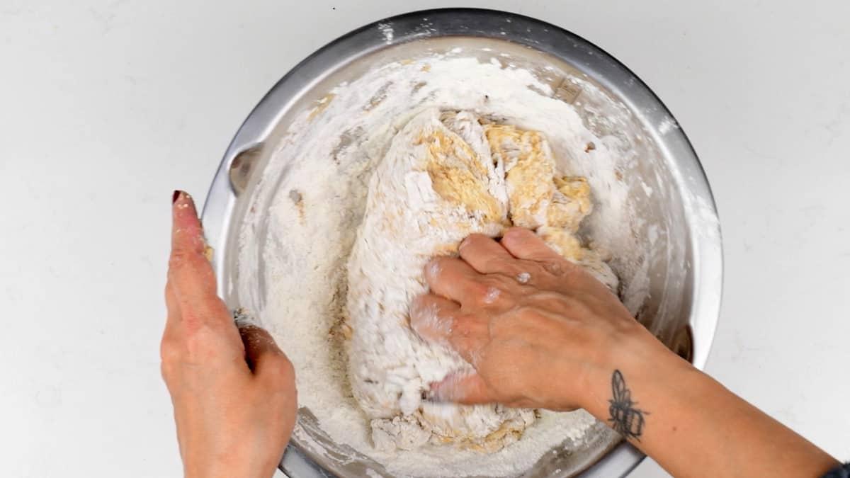 A hand mixing bread flour into the pumpkin sourdough mixture to form a shaggy dough.