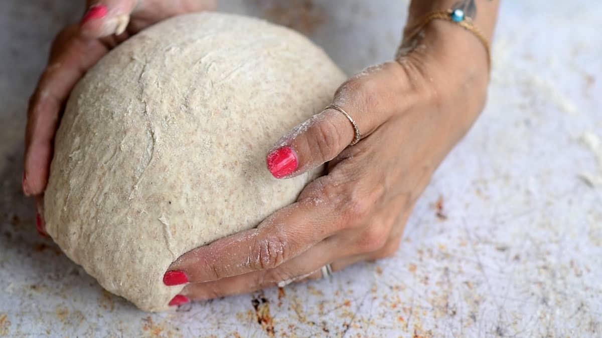 Close-up of hands shaping a ball of dough on a floured surface, preparing Quick Sourdough Bread With Yeast.