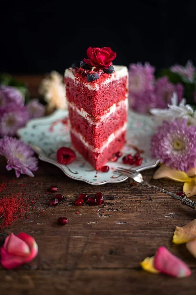 Slice of red velvet layer cake decorated with berries and flowers