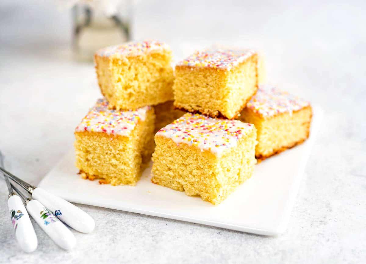 vanilla sheet cake cut into squares piled on a ceramic plate