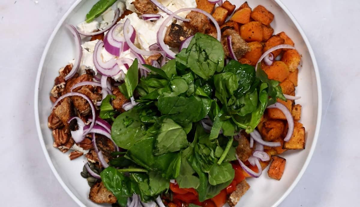 Ingredients for roasted butternut squash salad in a large bowl before tossing together
