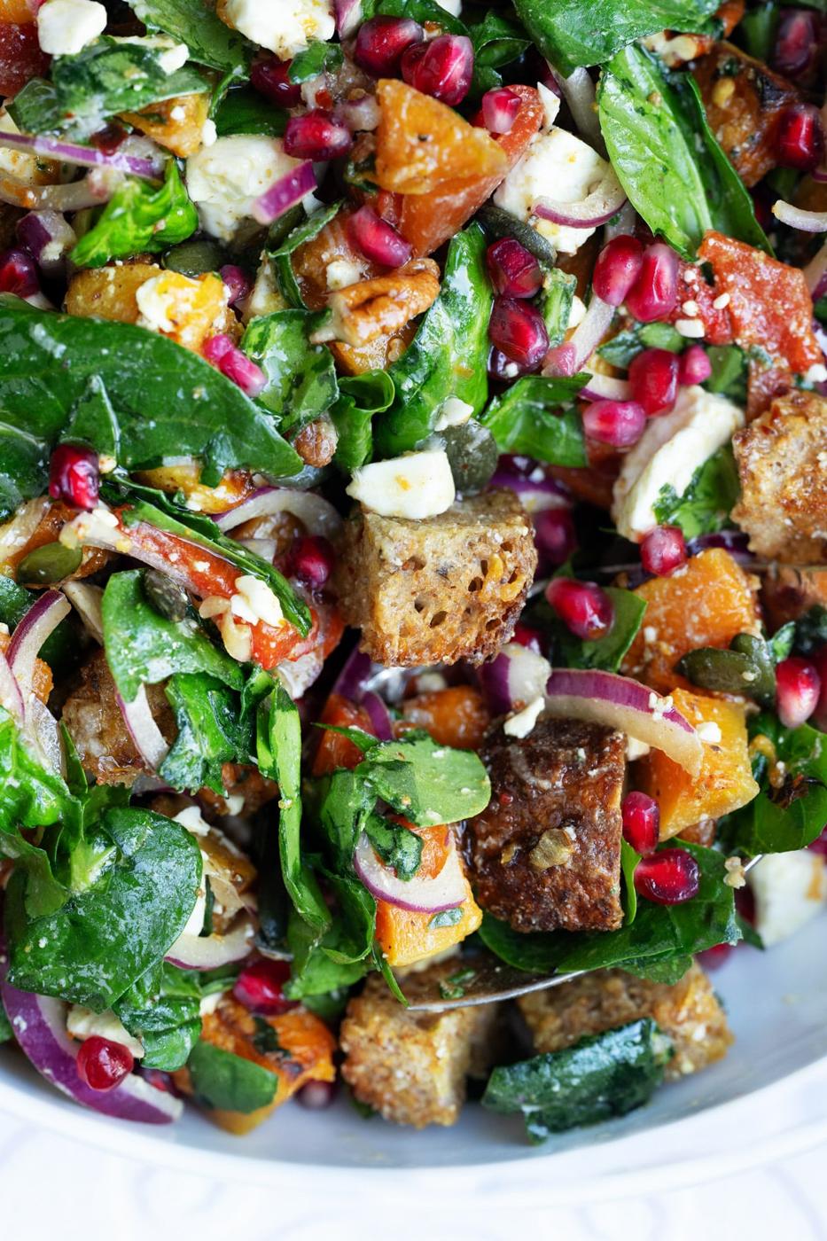close up on salad with butternut squash, spinach, feta, roasted peppers, croutons, pomegranate seeds