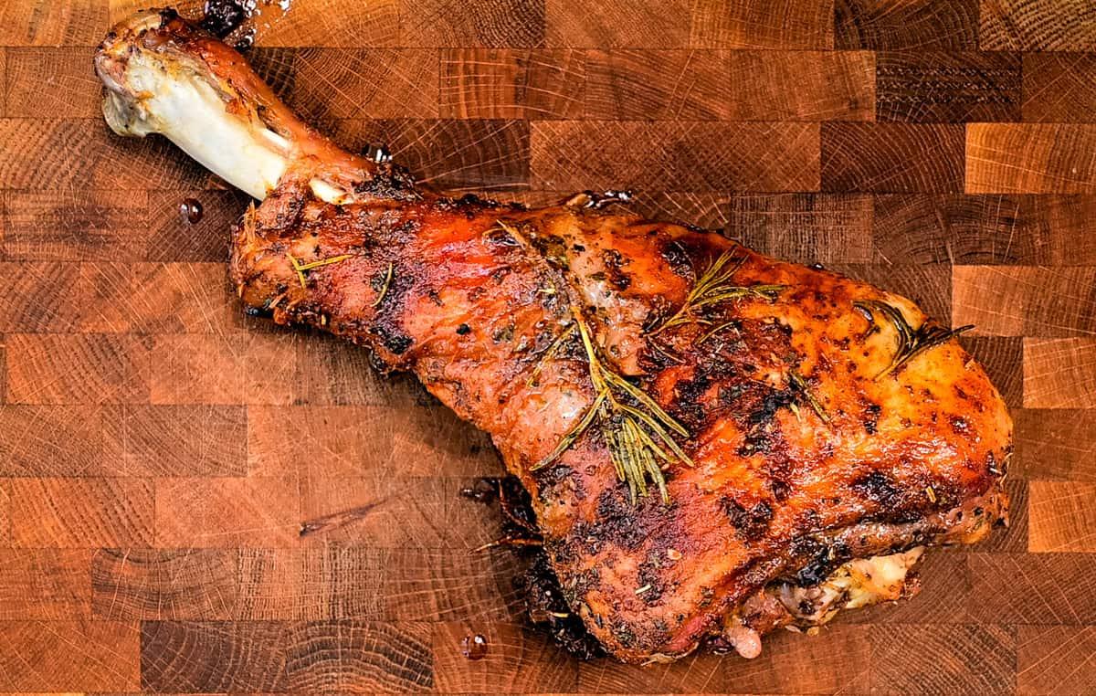 A roasted turkey leg with a crispy, golden-brown crust and sprigs of rosemary rests on a wooden cutting board