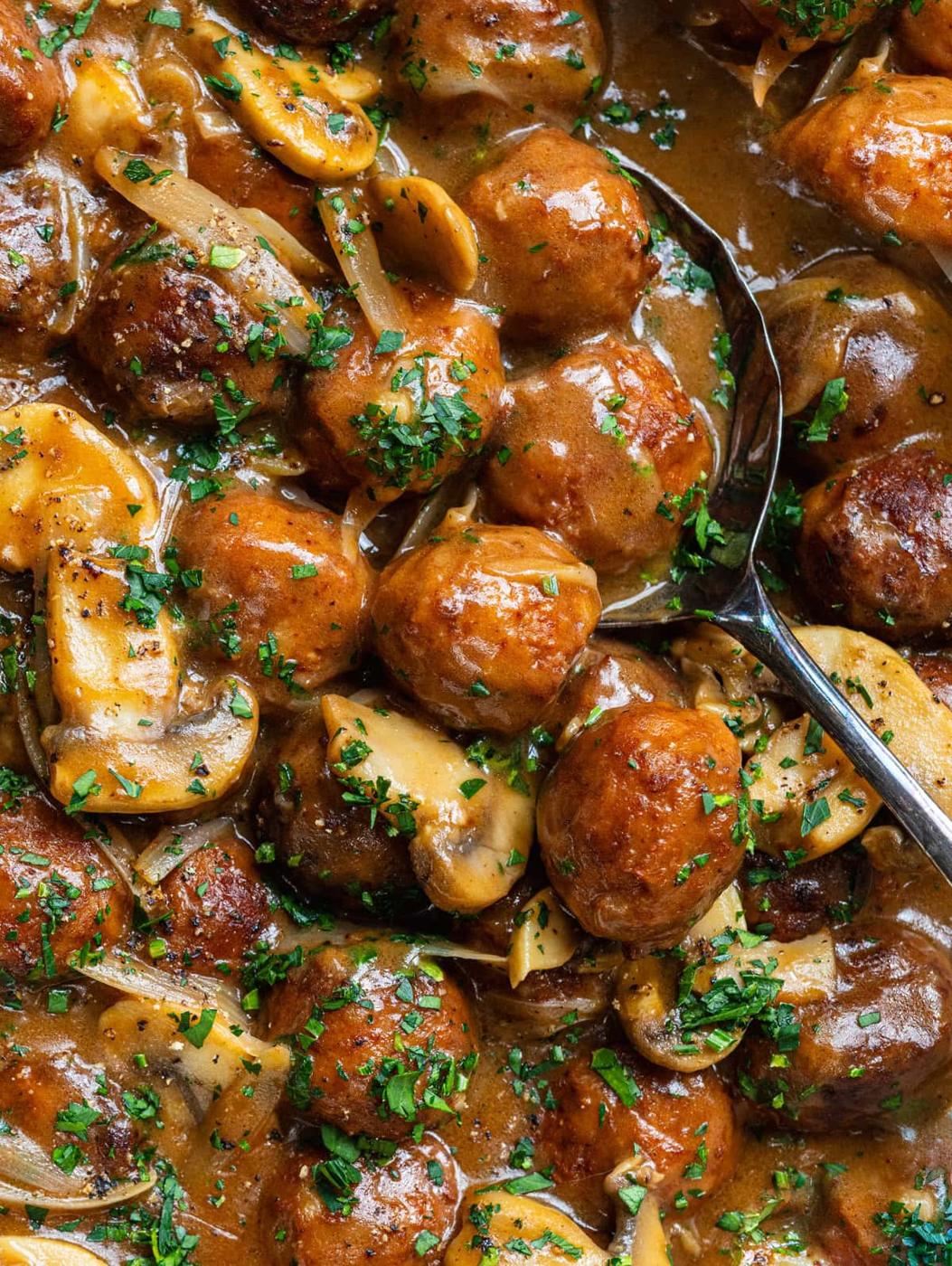 Salisbury Steak Meatballs in a rich brown gravy with sliced mushrooms and onions, garnished with chopped parsley. A metal spoon is partially visible in the dish.