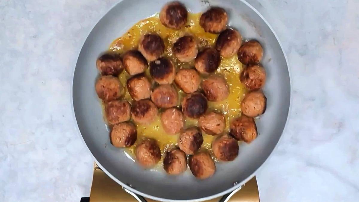 Browned Salisbury steak meatballs cooking in a skillet, viewed from above.