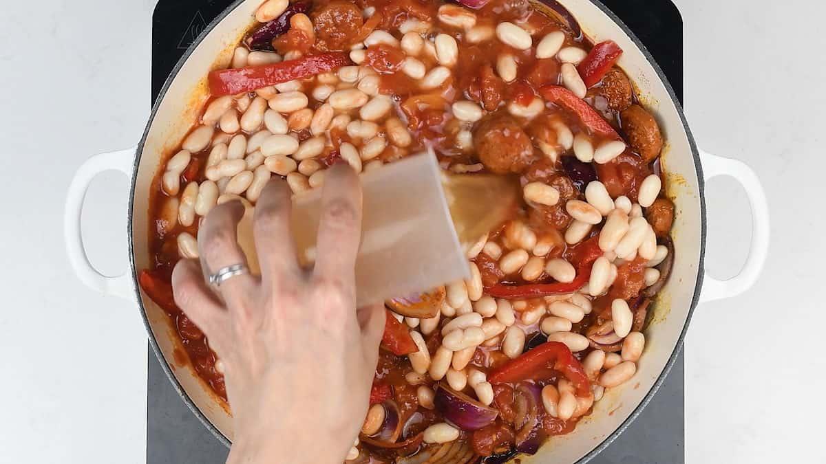 Making sausage and bean casserole in a large shallow cast iron pot