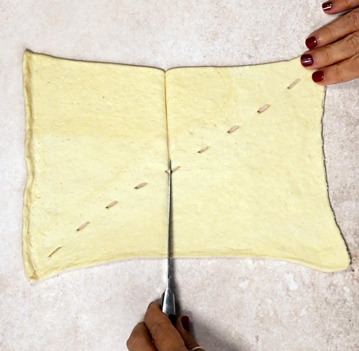 cutting a rectangular piece of crescent roll dough in half