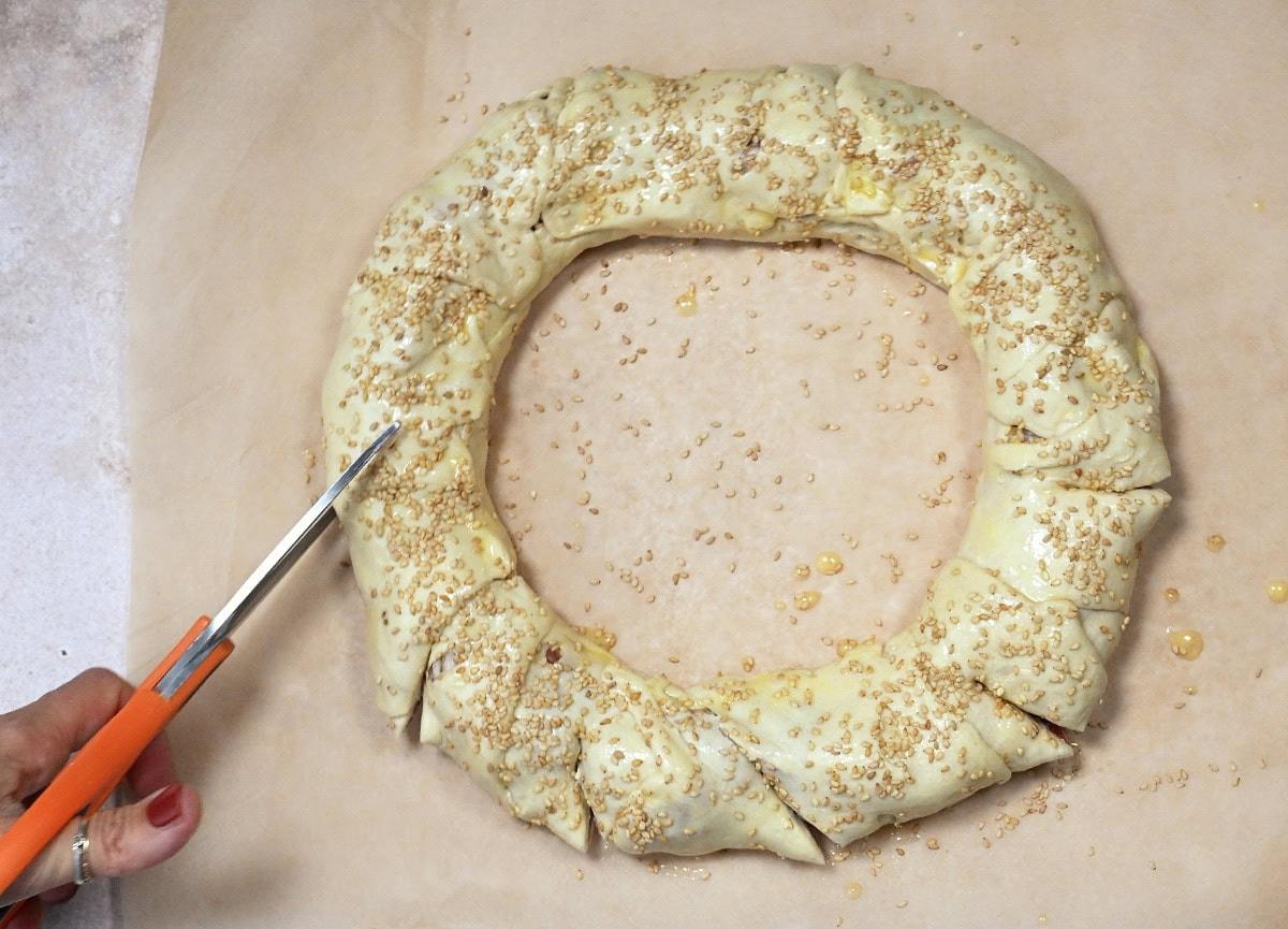 slicing into a sausage roll wreath topped with sesame seeds prior to baking