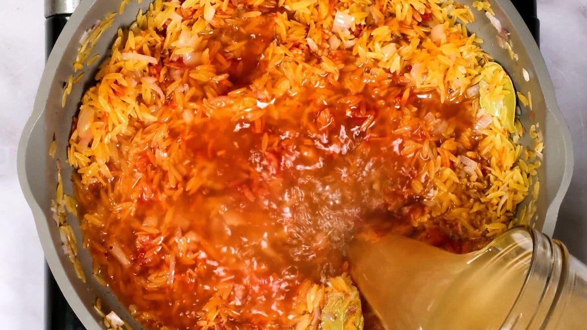 adding stock to a pan of orzo pasta
